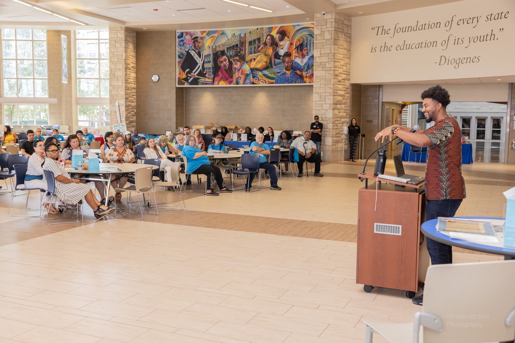 Ernest Crim III speaking to a seated audience in a school atrium